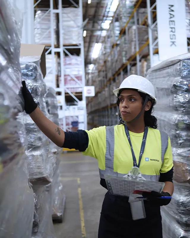 Employees with a forklift and a clipboard working between warehouse shelves.