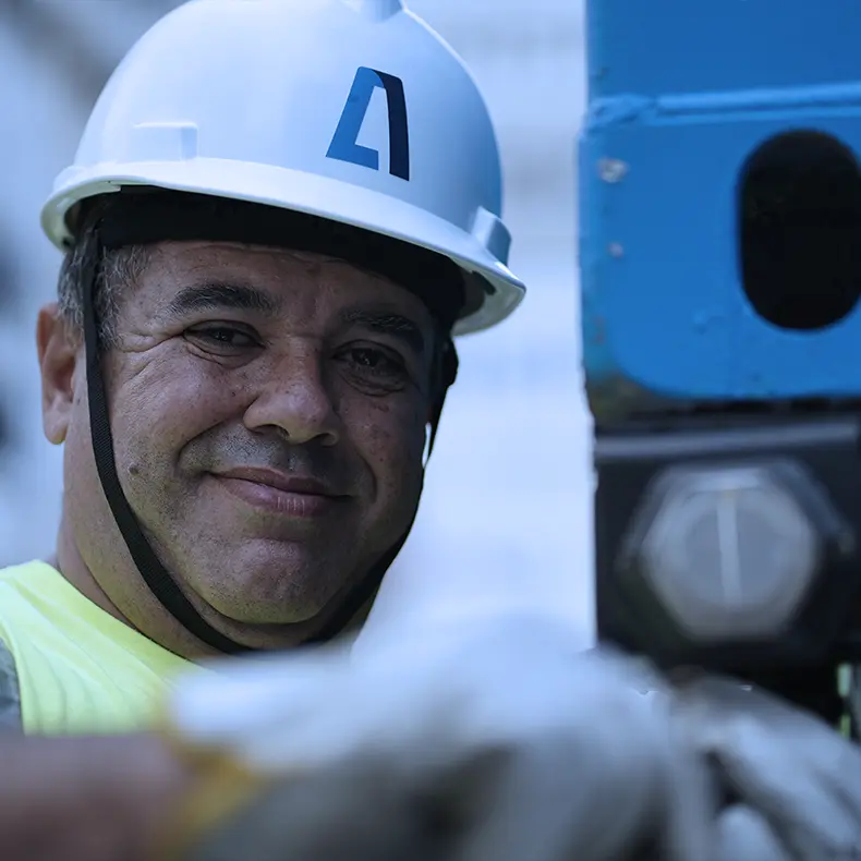 Operador da Aliança sorrindo, de capacete branco, ao lado de um contêiner.