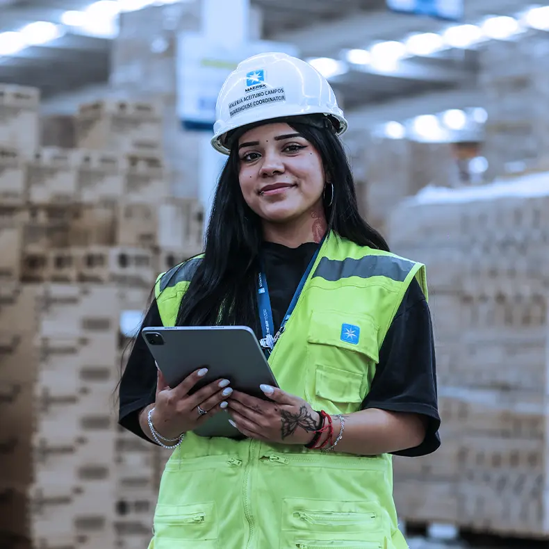 Colaboradora de capacete e colete refletivo usando um tablet em um armazém.