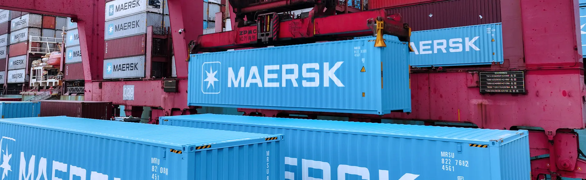 Contêineres Maersk sendo movimentados por guindaste em um terminal portuário.