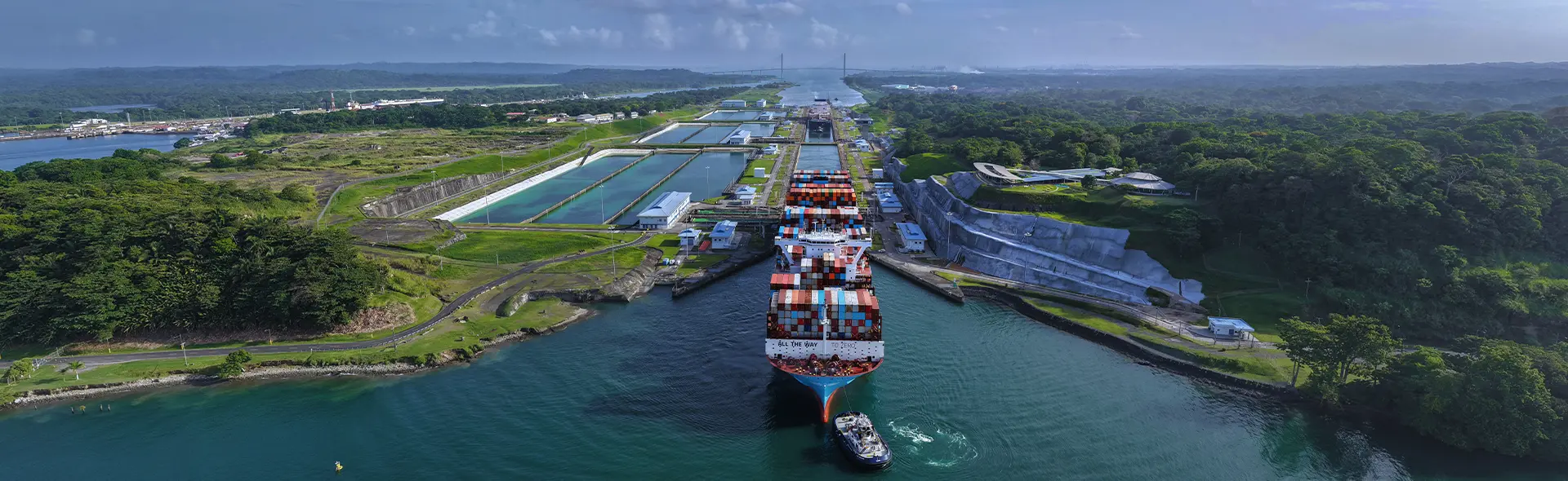 Navio porta-contêineres atravessando um canal cercado por mata.