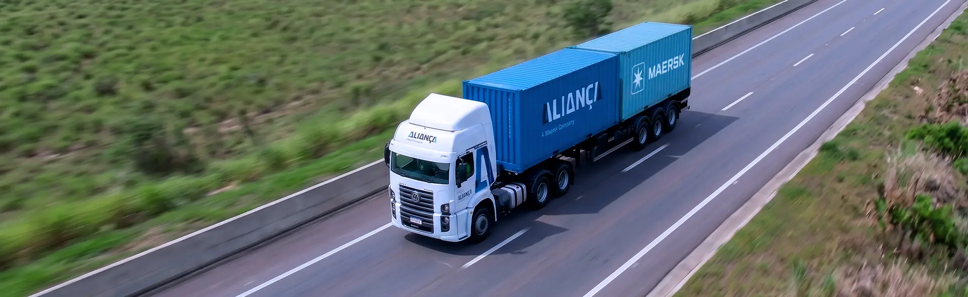 Caminhão da Aliança com contêineres Aliança e Maersk em uma rodovia.